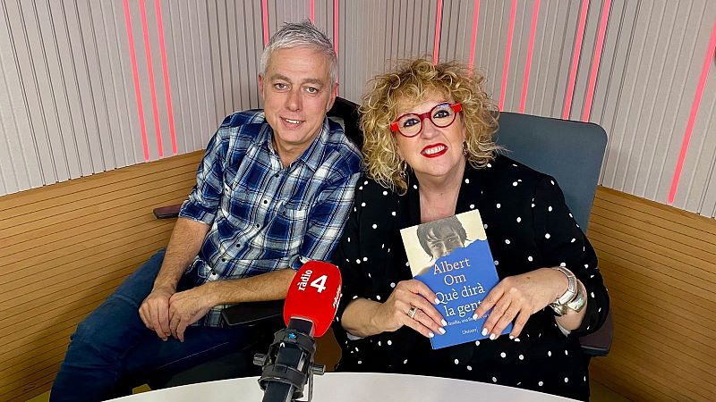 Dos personas en un estudio de radio con paneles de madera; ella sostiene el libro de Albert Om y �l viste camisa a cuadros junto a un micr�fono con el logo de r�dio 4.