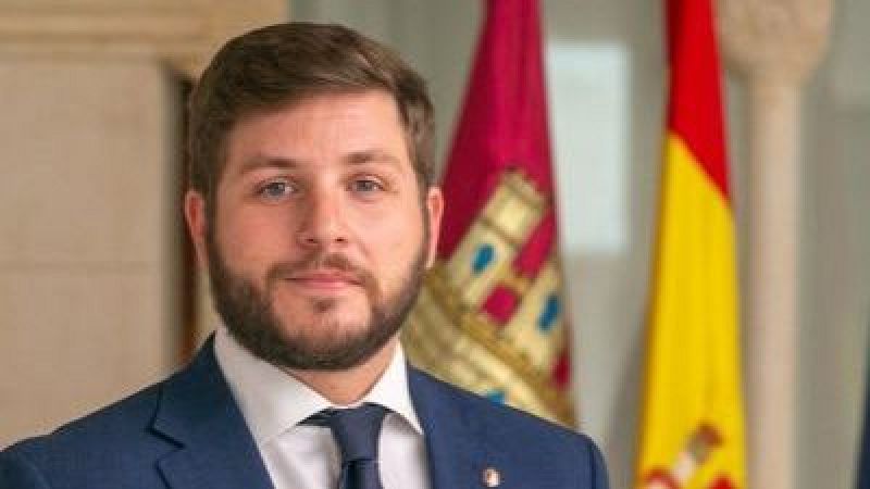 Retrato institucional de Nacho Hernando con traje azul, camisa blanca y corbata, con las banderas de España y Castilla-La Mancha de fondo.