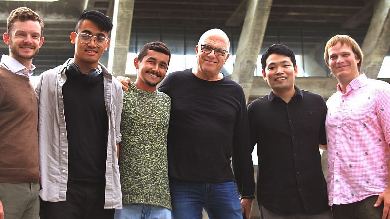 Plano medio de seis hombres sonrientes posando juntos frente a una estructura arquitect�nica de hormig�n, incluyendo al director Steven Schick en el centro.