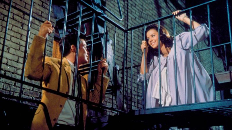 Fotograma de una escena rom�ntica nocturna donde una mujer sonr�e desde una escalera de incendios a un hombre que la mira desde abajo.
