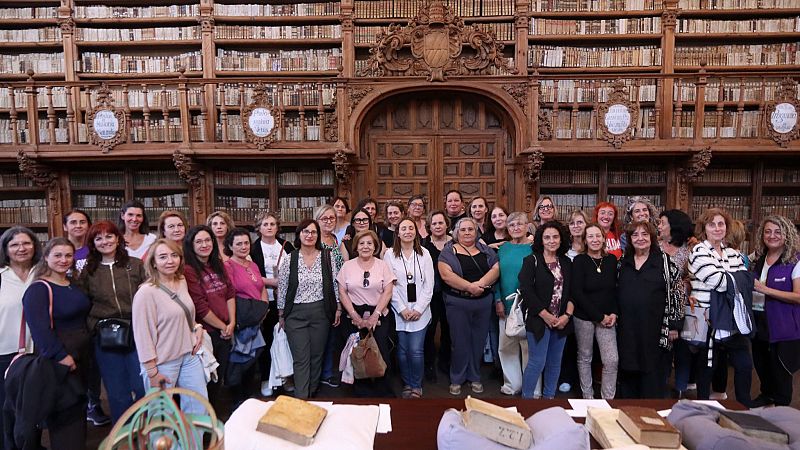 Grupo de mujeres sonrientes posando en el interior de una histórica biblioteca con estanterías de madera, libros antiguos y una puerta monumental.