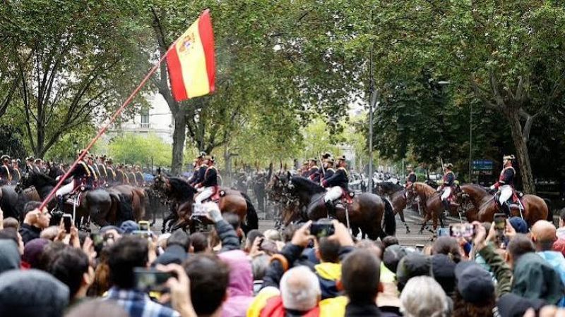 Espectadores de espaldas graban con m�viles un desfile militar con caballer�a en una amplia avenida de Madrid, destacando una bandera de Espa�a.