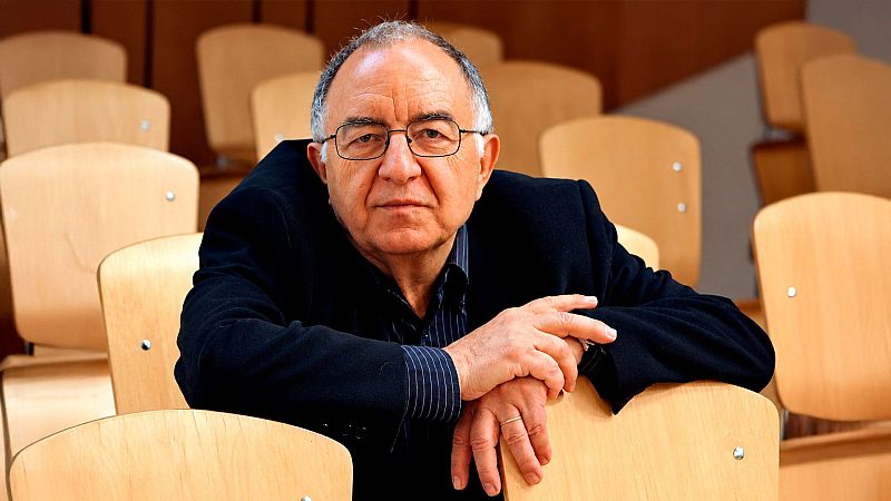 Plano medio del historiador Ricardo Garc�a C�rcel con gafas, serio y reflexivo, apoyado en el respaldo de una silla de madera en un auditorio.