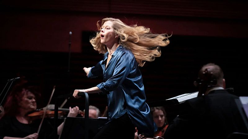 La directora Barbara Hannigan dirige con energ�a e intensidad en un auditorio, rodeada por m�sicos de una orquesta sinf�nica.