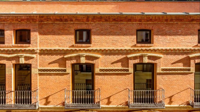 Fachada exterior de ladrillo visto con balcones y detalles arquitectónicos de estilo tradicional madrileño.