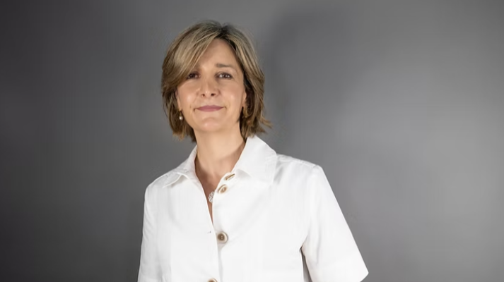 Retrato en plano medio corto de la periodista Mamen Asencio con camisa blanca y fondo gris.