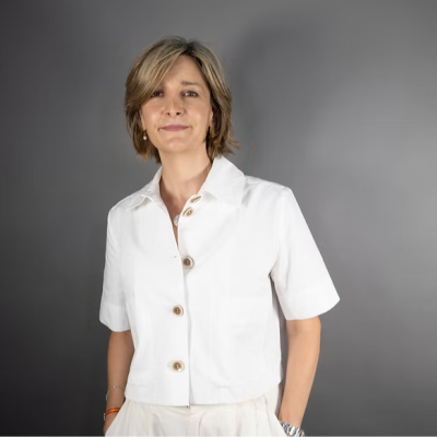 Retrato en plano medio corto de la periodista Mamen Asencio con camisa blanca y fondo gris.