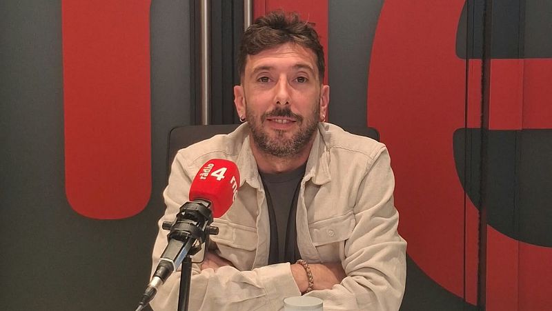 Marc Llibre sonr�e a la c�mara en un estudio de radio, con los brazos cruzados sobre la mesa junto a un micr�fono con funda roja.