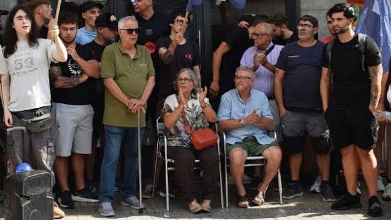 Concentraci�n solidaria de vecinos y activistas frente a un edificio, con personas mayores aplaudiendo en el centro y un grupo de apoyo rode�ndolas.