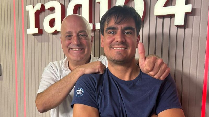 Dos hombres sonr�en en un estudio de radio con paneles de madera y el r�tulo luminoso r�dio 4 al fondo.