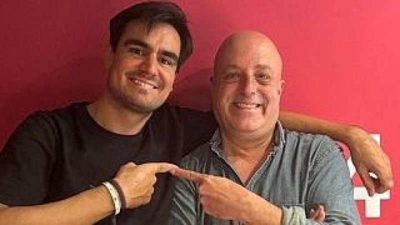 Dos hombres sonrientes posan ante un fondo magenta, mostrando complicidad al se�alarse con el dedo �ndice hacia el centro.