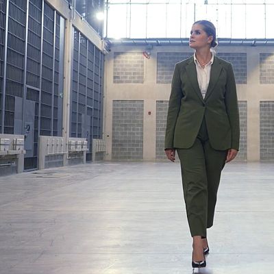Laura Fernández camina con traje verde oliva por un pasillo entre celdas en una moderna prisión.