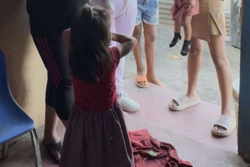 Grupo de personas en el umbral de una vivienda sencilla, destacando una ni�a de espaldas en primer plano y diversas personas alrededor cuyas caras no se ven, dentro de un contexto social de Radio Nacional de Espa�a.