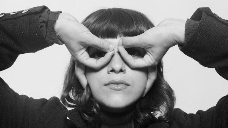 Retrato en blanco y negro de una mujer joven mirando a trav�s de los c�rculos formados con sus dedos frente a sus ojos.