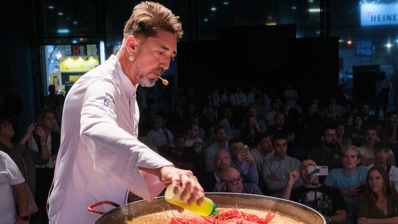 El chef Quique Dacosta añade aceite con un dosificador sobre una paella con arroz y gambas rojas en un showcooking.