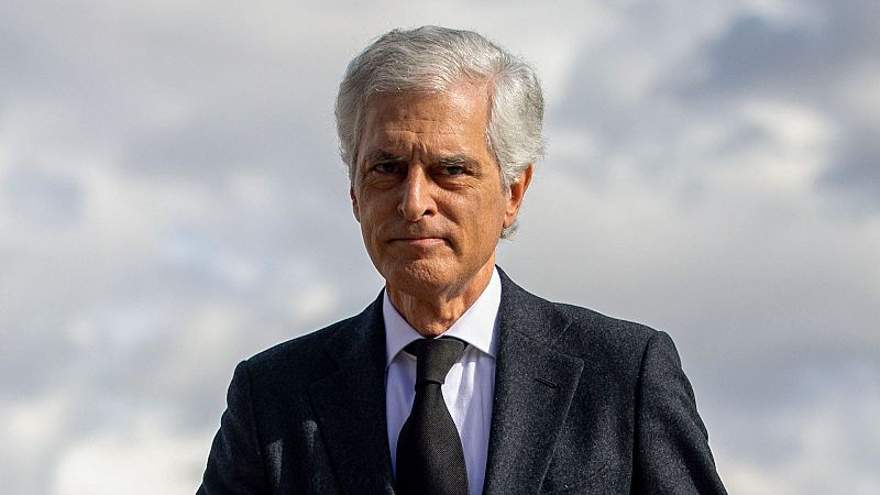 Plano medio corto de Adolfo Su�rez Illana con expresi�n seria, traje oscuro, camisa blanca y corbata negra ante un fondo desenfocado.
