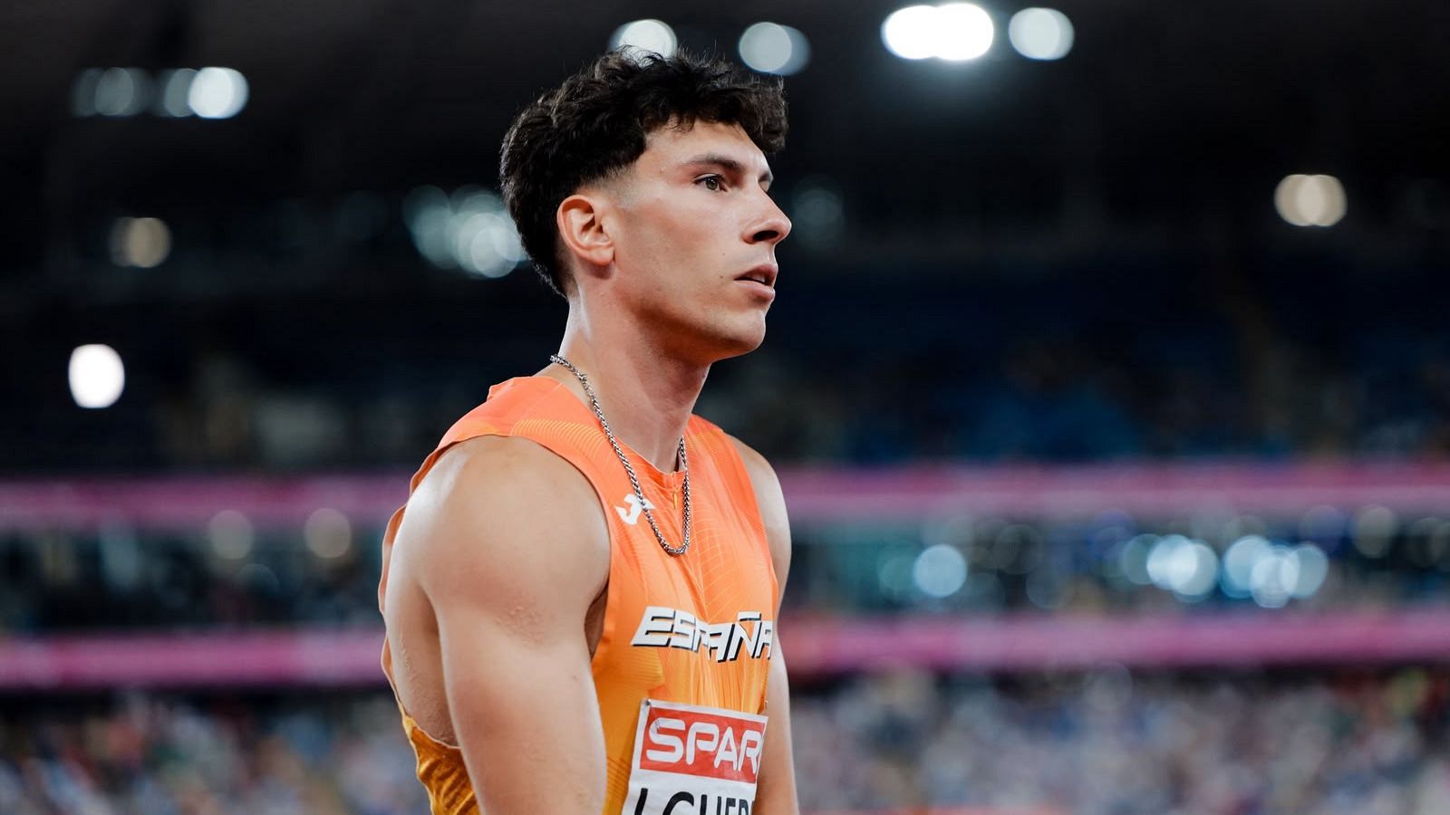 Plano medio del atleta Jaime Guerra con camiseta naranja de Espa�a y dorsal SPAR en un estadio iluminado de noche.