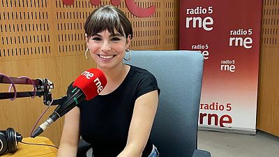 La escritora Andrea Abreu sonr�e sentada en un estudio de radio, vistiendo camiseta negra y aros, con un micr�fono de RNE en primer plano y paneles ac�sticos de fondo.