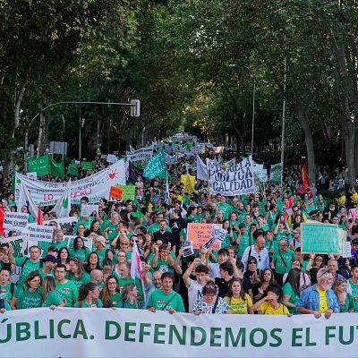 Manifestación multitudinaria en una avenida urbana arbolada donde los asistentes portan una pancarta blanca con la inscripción «LA PÚBLICA. DEFENDEMOS EL FUTURO.» y múltiples carteles reivindicativos.