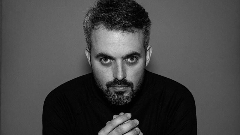Retrato en blanco y negro de un hombre con barba corta y expresi�n seria que apoya las manos entrelazadas bajo la barbilla.