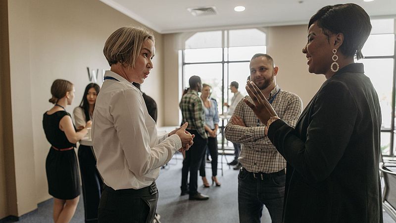 Tres profesionales conversan animadamente en una sala corporativa luminosa durante un evento de networking.
