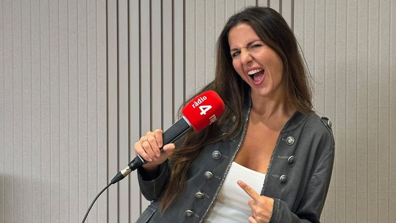 La periodista Georgina Badenas sonr�e en un estudio de grabaci�n sosteniendo un micr�fono de R�dio 4 y apunt�ndose al pecho.