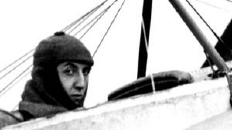 Fotografía histórica en blanco y negro de un aviador con gorro de vuelo asomado a la cabina abierta de un biplano.
