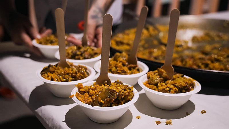 Cuencos blancos con raciones individuales de paella y cucharas de madera sobre un mantel, en un evento gastronómico.