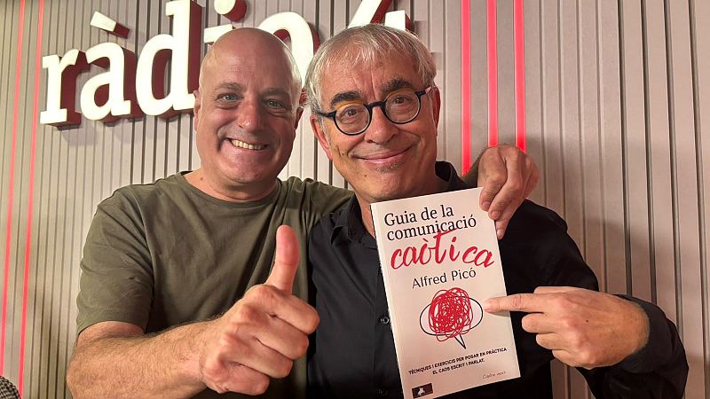 Dos hombres sonrientes en un estudio de radio; el de la derecha muestra el libro �Guia de la comunicaci� ca�tica� y el de la izquierda hace el gesto de aprobaci�n con el pulgar.