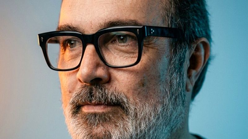 Primer plano de un hombre maduro con barba y gafas, iluminado con un contraste de luces cálidas y frías.