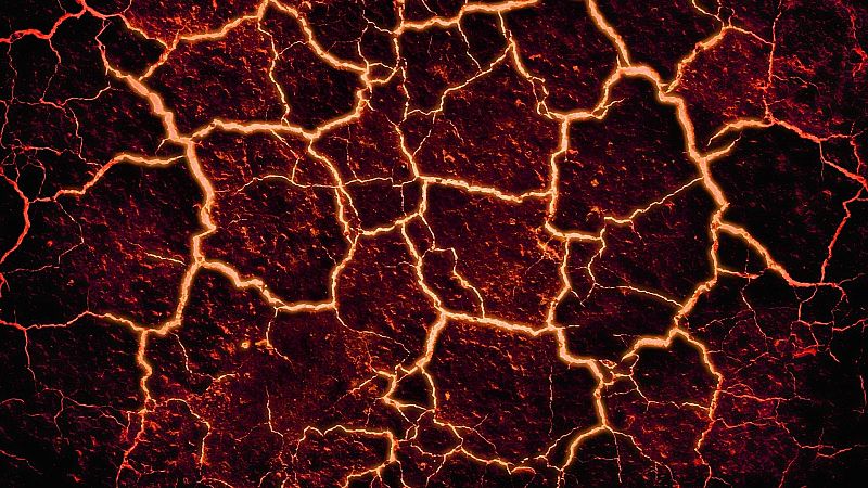 Superficie de roca volcánica oscura con profundas grietas iluminadas por un brillo incandescente de tonos anaranjados y rojizos.