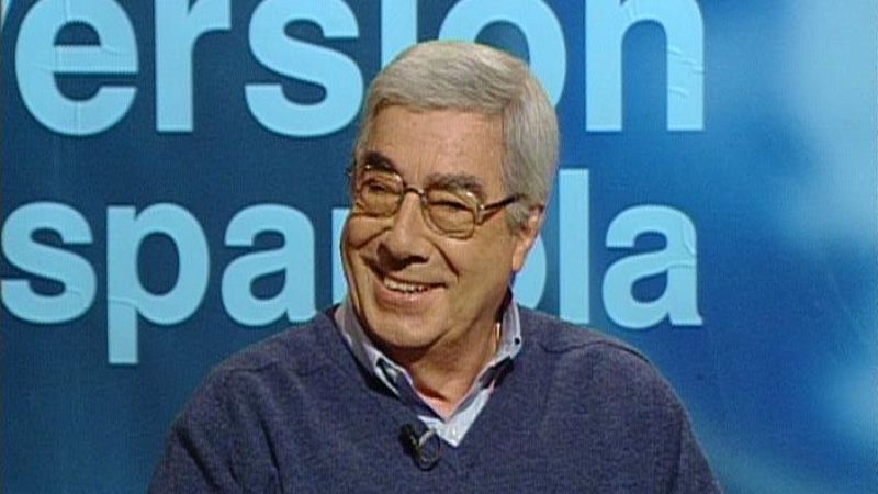 El guionista Rafael Azcona sonríe de forma relajada en un plató de televisión con un panel azul al fondo.
