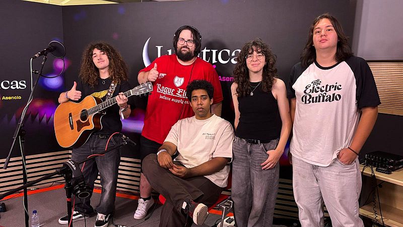 Cinco jóvenes músicos posan junto al equipo en un estudio de radio con un panel corporativo de fondo.