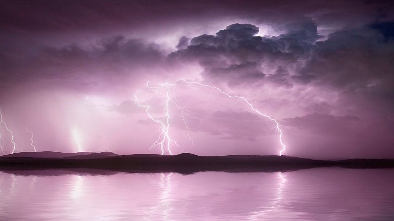 Tormenta el�ctrica nocturna sobre un lago tranquilo con rayos viol�ceos y reflejos en el agua.