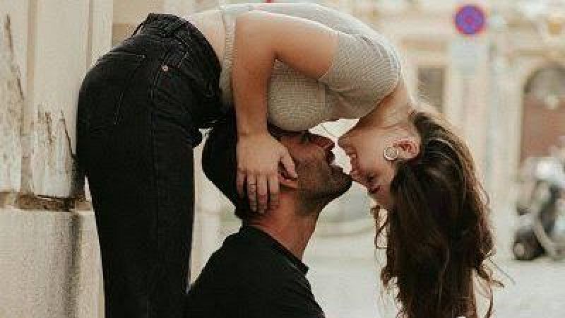 Pareja joven compartiendo un momento afectuoso al aire libre, mir�ndose sonrientes y a punto de besarse con una calle adoquinada al fondo.
