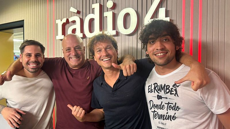 Cuatro hombres sonrientes posan abrazados en un estudio de radio iluminado con neones rojos y paneles de madera.