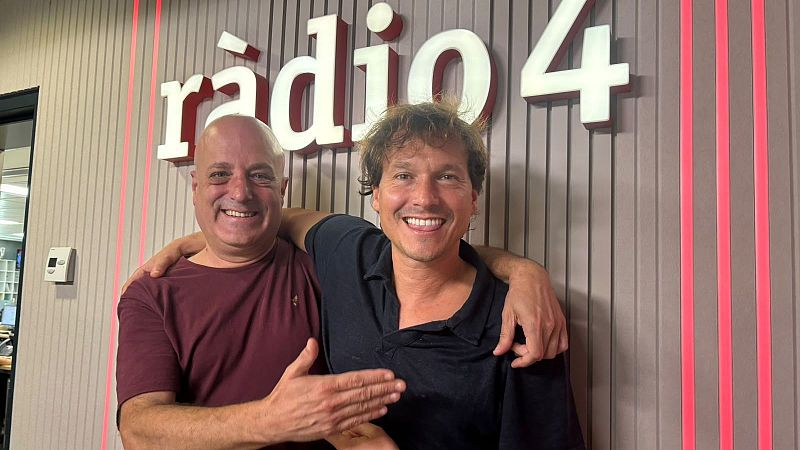 Dos hombres sonrientes posan en los estudios de R�dio 4, con el cantautor Ramon Mirabet a la derecha y un hombre calvo a la izquierda frente a una pared con paneles y luces rojas.