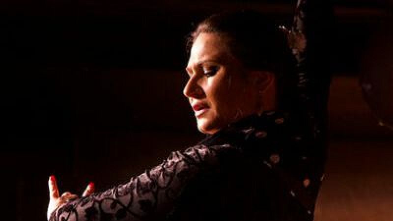 La bailaora Karime Amaya realiza una intensa actuación de flamenco con traje negro de encaje y expresión concentrada bajo una iluminación teatral.