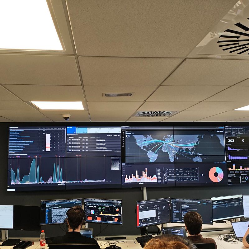 Centro de operaciones de seguridad con analistas ante pantallas que muestran mapas de ciberataques y gráficos de datos.