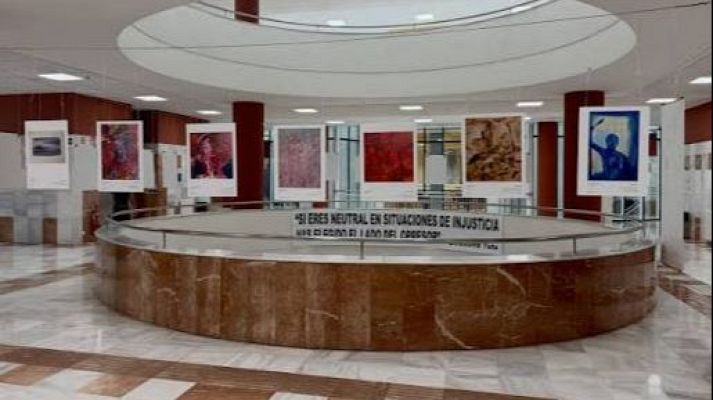 Vestíbulo universitario luminoso con suelo de mármol, instalación artística colgante y una pancarta con una cita de Desmond Tutu en la barandilla central.