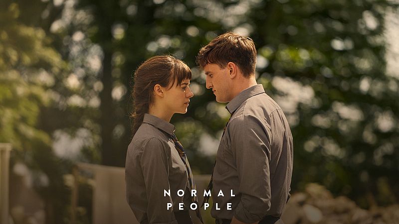 Dos jóvenes, él y ella, se miran intensamente en una imagen promocional de 'Normal People'. Ambos visten camisas grises y tienen el pelo oscuro. Fondo borroso.