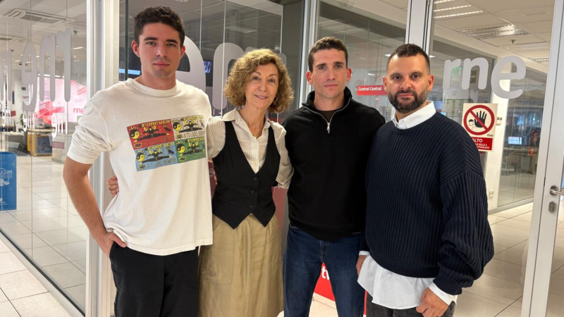 Cuatro personas posan sonrientes en el interior de una emisora de radio con paredes acristaladas y logotipos corporativos.