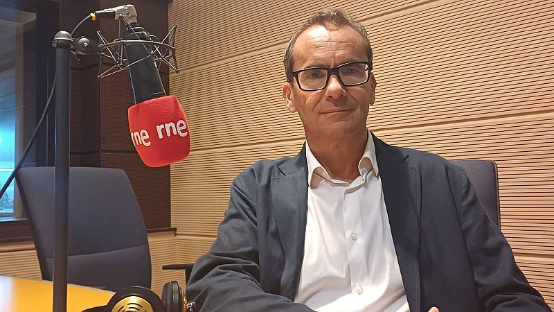 El periodista David Jiménez aparece en un estudio de radio con micrófono de espuma roja y auriculares, sobre un fondo de paneles acústicos de madera.