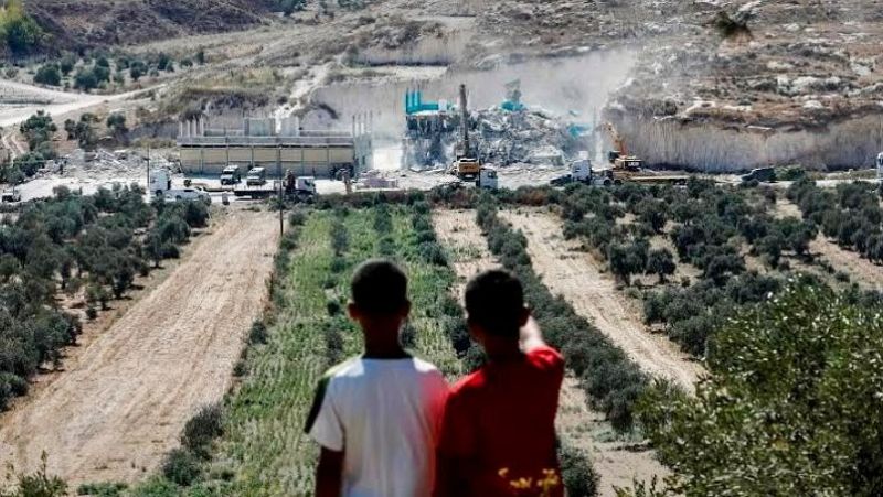 Dos ni�os contemplan desde una colina un paisaje rural �rido con olivos y una obra de demolici�n al fondo.