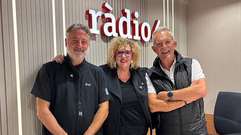 Tres personas sonrientes posan en un estudio de radio con paneles de madera y un logotipo iluminado al fondo.