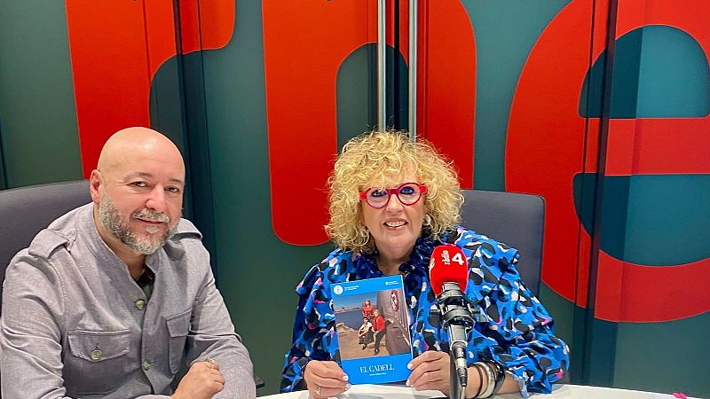 Josep Maria Mir� y una mujer posan sonrientes en el estudio de R�dio 4 sosteniendo un ejemplar de 'El cadell', con un micr�fono corporativo en primer plano.