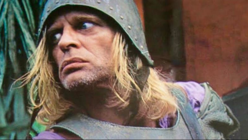 Primer plano del actor Klaus Kinski con casco y armadura, mostrando una intensa mirada desorbitada y expresi�n de locura en un entorno tropical.