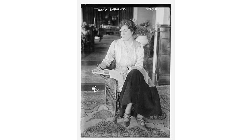 Retrato en blanco y negro de la soprano Mar�a Barrientos sentada en un sill�n leyendo una partitura sobre una alfombra ornamental.
