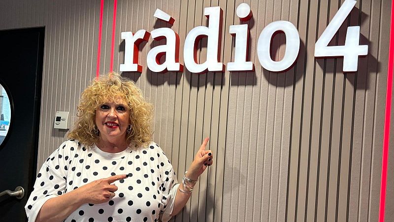 La periodista S�lvia Tarragona sonr�e en el estudio de radio, se�alando hacia el gran logotipo luminoso de R�dio 4 en la pared.