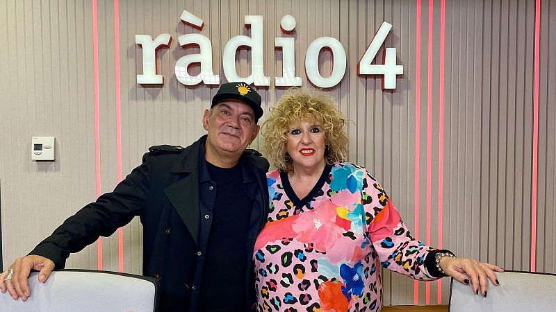 Dos personas posan sonrientes en un estudio de radio frente al logotipo iluminado de r�dio 4, acompa�ados por mobiliario de oficina y luces ambientales rojas.